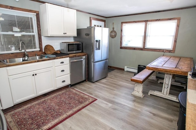 kitchen with light wood finished floors, a sink, decorative backsplash, stainless steel appliances, and a baseboard radiator