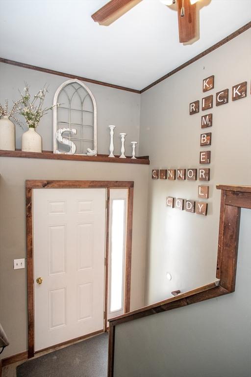 carpeted entrance foyer featuring ornamental molding and a ceiling fan