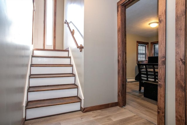 stairway featuring baseboard heating, baseboards, and wood finished floors