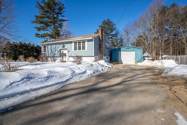 bi-level home featuring driveway, a detached garage, fence, an outdoor structure, and a chimney