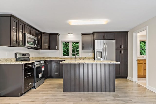 43 Water St, Freetown, MA 02702 - kitchen with stainless steel appliances, light wood-style floors, light stone counters, a center island, and glass insert cabinets