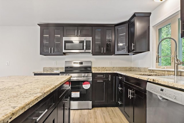 43 Water St, Freetown, MA 02702 - kitchen featuring appliances with stainless steel finishes, a sink, light stone countertops, glass insert cabinets, and light wood-style floors