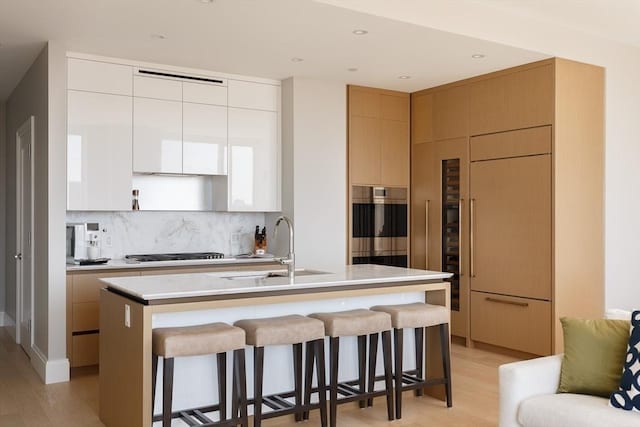 kitchen featuring sink, a kitchen breakfast bar, stainless steel gas stovetop, a kitchen island with sink, and white cabinets