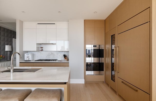 kitchen with sink, appliances with stainless steel finishes, light stone counters, light hardwood / wood-style floors, and a kitchen bar