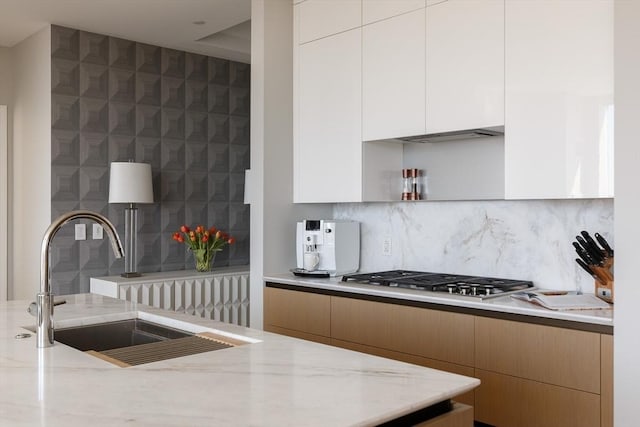 kitchen featuring sink, white cabinetry, backsplash, light stone counters, and stainless steel gas stovetop