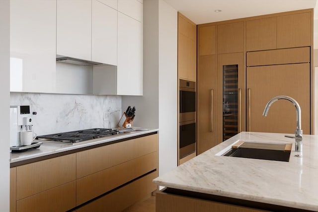 kitchen featuring sink, stainless steel appliances, tasteful backsplash, light stone countertops, and white cabinets