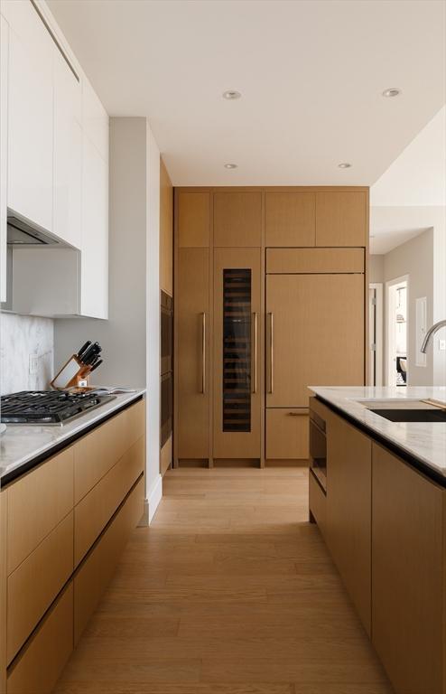 kitchen with appliances with stainless steel finishes, sink, wine cooler, decorative backsplash, and light wood-type flooring