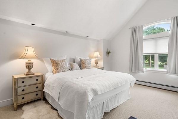 bedroom with a baseboard heating unit, multiple windows, light colored carpet, and vaulted ceiling