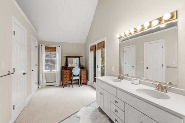 full bath featuring lofted ceiling, double vanity, baseboard heating, and a sink