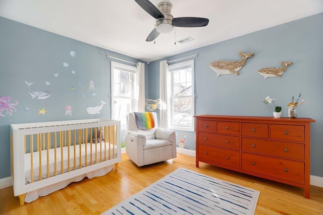 bedroom featuring a crib, light hardwood / wood-style flooring, and ceiling fan