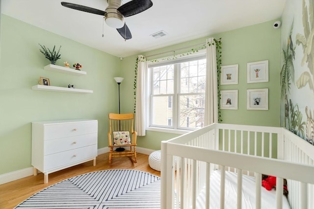 bedroom with ceiling fan, a nursery area, and light wood-type flooring