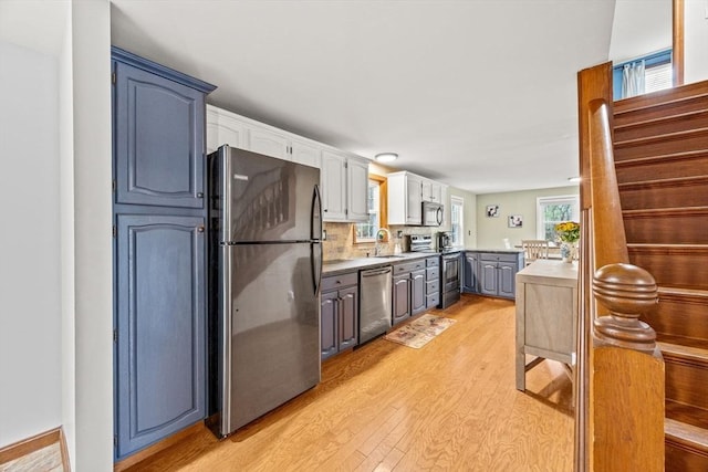 kitchen with backsplash, sink, light hardwood / wood-style flooring, blue cabinetry, and stainless steel appliances