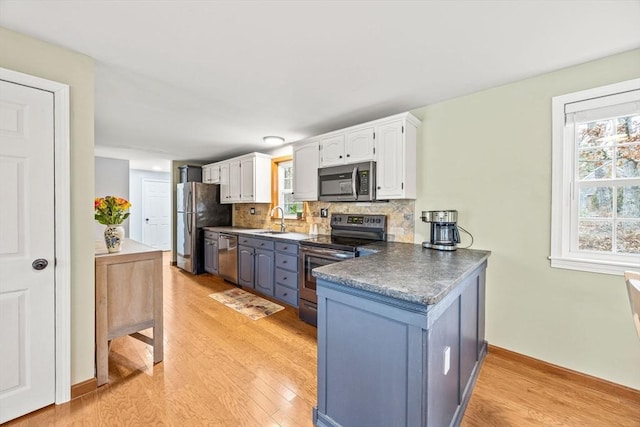 kitchen with appliances with stainless steel finishes, backsplash, sink, light hardwood / wood-style flooring, and white cabinetry