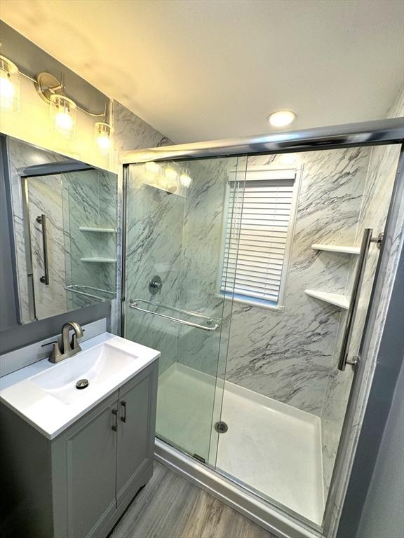 bathroom featuring wood finished floors, a marble finish shower, and vanity