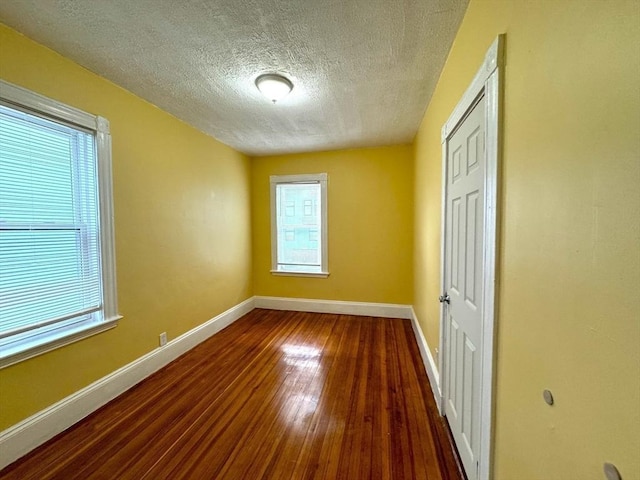 spare room with a textured ceiling, wood finished floors, and baseboards