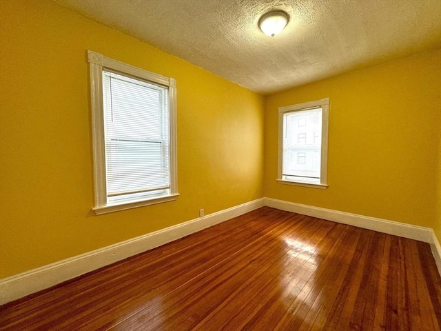 empty room featuring hardwood / wood-style floors, baseboards, and a textured ceiling