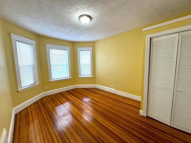 unfurnished bedroom featuring a textured ceiling, a closet, wood-type flooring, and baseboards