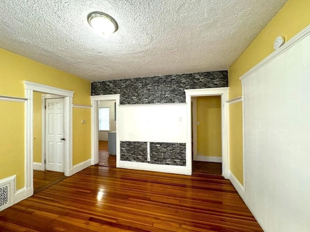 spare room with a textured ceiling, wood finished floors, visible vents, and baseboards