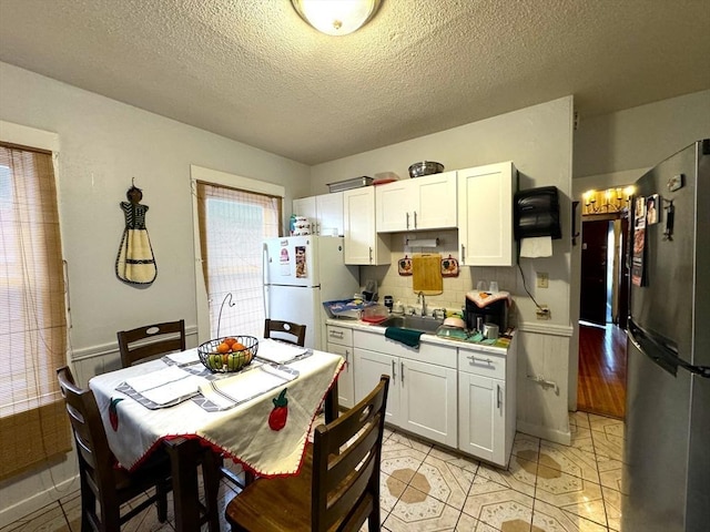 kitchen featuring freestanding refrigerator, light countertops, a sink, and white cabinetry