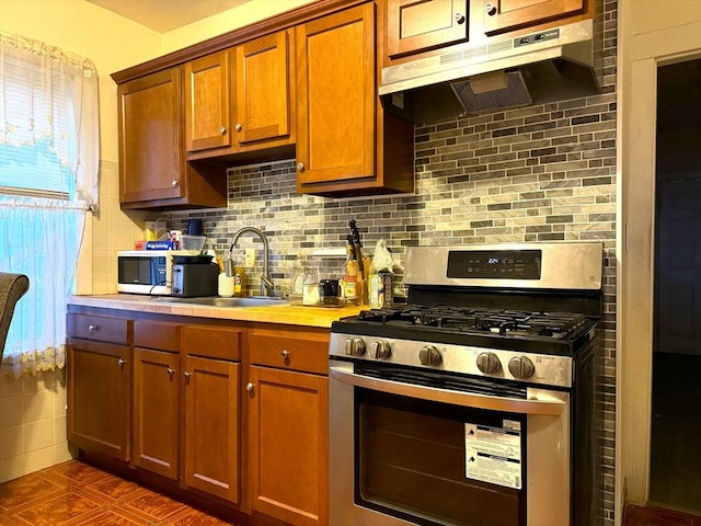 kitchen with light countertops, stainless steel range with gas stovetop, a sink, and under cabinet range hood