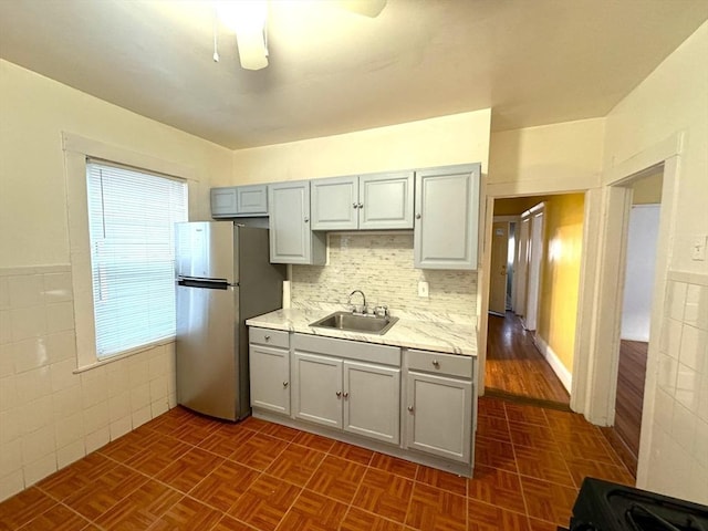 kitchen featuring light countertops, gray cabinetry, freestanding refrigerator, wainscoting, and a sink