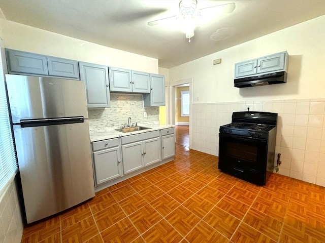 kitchen featuring black gas range, gray cabinetry, under cabinet range hood, a sink, and freestanding refrigerator