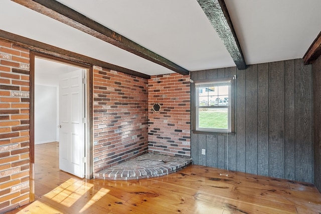 unfurnished room with beamed ceiling, wooden walls, and light wood-type flooring