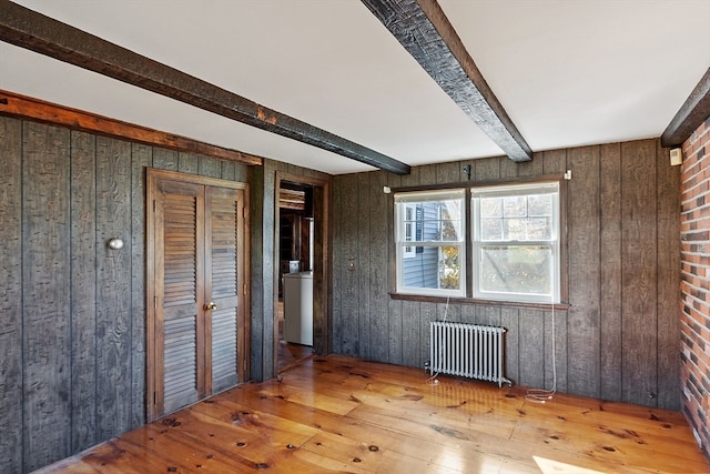 spare room featuring washer / dryer, wood-type flooring, radiator, wooden walls, and beam ceiling