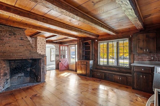 unfurnished living room with beam ceiling, wooden ceiling, light wood-type flooring, and a brick fireplace