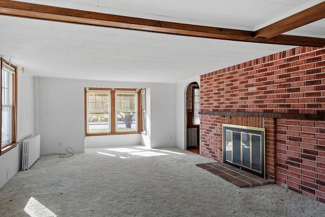 unfurnished living room with radiator, beam ceiling, carpet flooring, and a brick fireplace