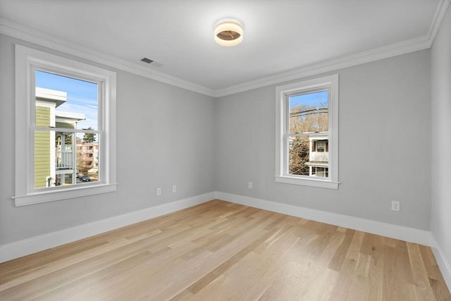 spare room featuring a healthy amount of sunlight, ornamental molding, and light hardwood / wood-style flooring