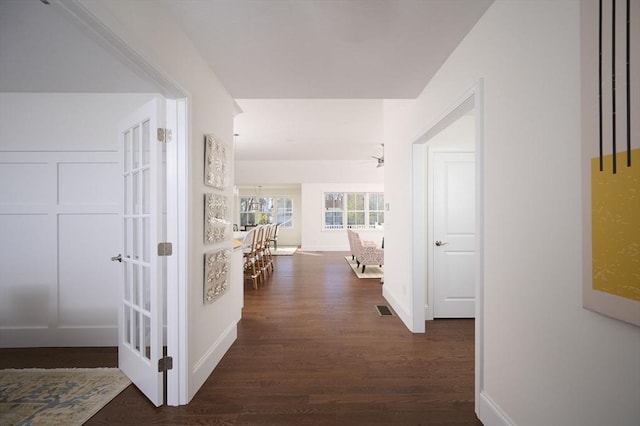 hall featuring dark wood-style flooring, visible vents, and baseboards