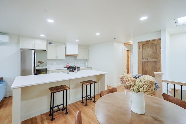 307 E Eagle St, Boston, MA 02128 - kitchen featuring appliances with stainless steel finishes, decorative backsplash, a kitchen breakfast bar, white cabinets, and an AC wall unit