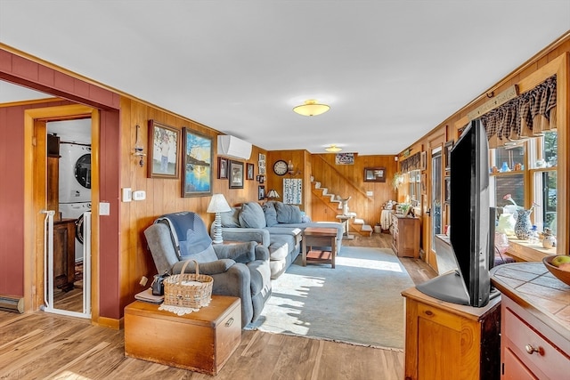 living room with stacked washer and clothes dryer, light wood-type flooring, a wall unit AC, and wood walls