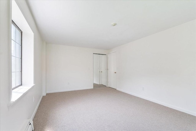 empty room featuring light carpet, baseboards, and a baseboard radiator