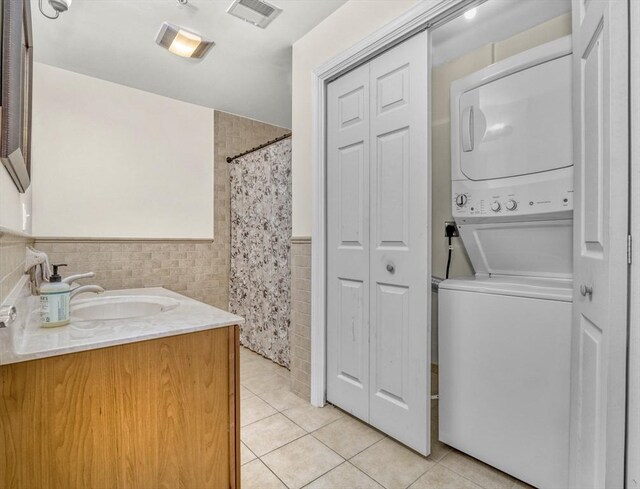 laundry room with stacked washer / dryer, sink, light tile patterned floors, and tile walls