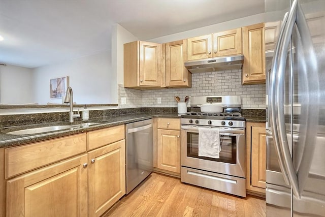 kitchen with appliances with stainless steel finishes, light hardwood / wood-style floors, dark stone counters, and sink