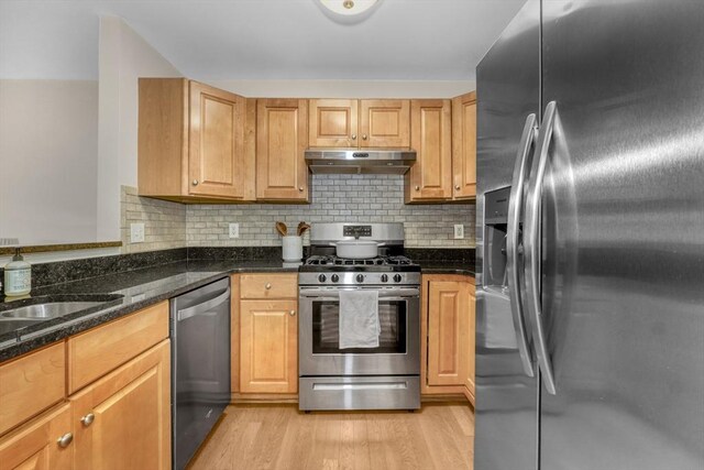 kitchen featuring decorative backsplash, appliances with stainless steel finishes, light wood-type flooring, dark stone counters, and sink