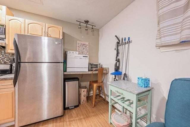 kitchen featuring light wood finished floors, tasteful backsplash, light countertops, light brown cabinetry, and freestanding refrigerator