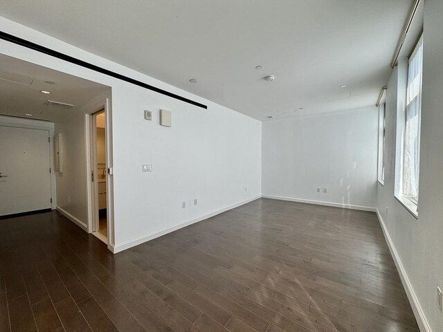 spare room featuring dark wood-style flooring and baseboards