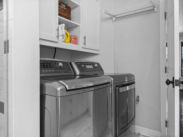 washroom featuring washing machine and dryer, cabinet space, and baseboards