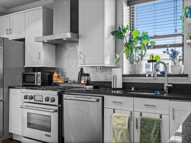 kitchen with appliances with stainless steel finishes, wall chimney range hood, a sink, tasteful backsplash, and white cabinetry