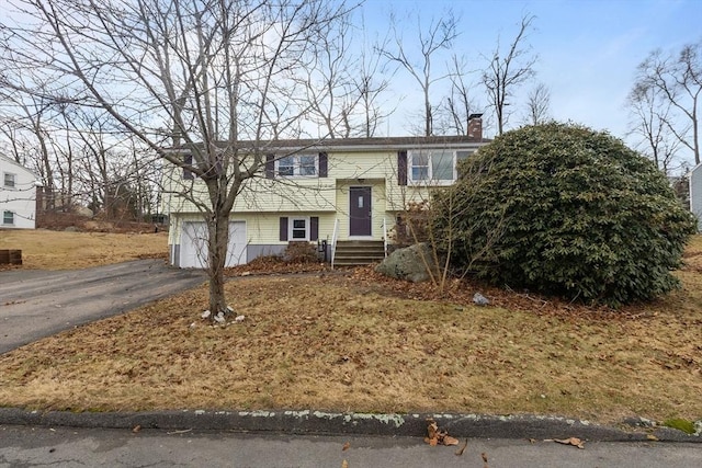 split foyer home featuring aphalt driveway, a garage, and a chimney