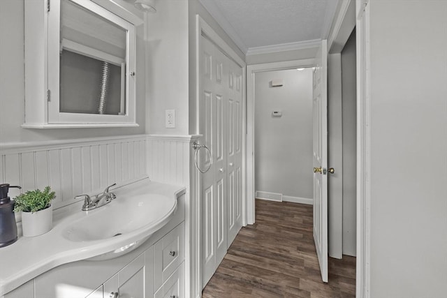 bathroom featuring vanity, wood finished floors, a wainscoted wall, ornamental molding, and a textured ceiling