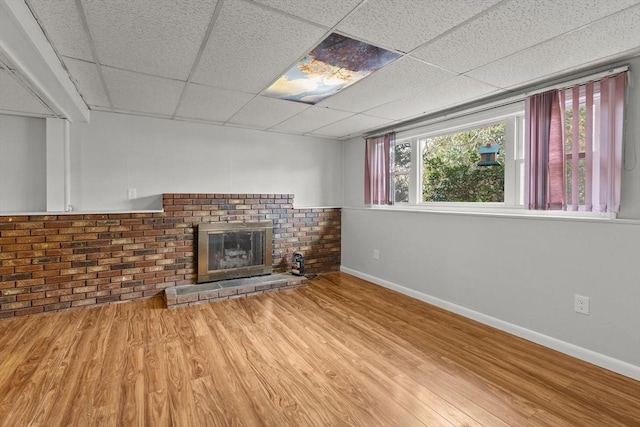 unfurnished living room featuring a drop ceiling, a brick fireplace, baseboards, and wood finished floors