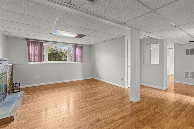 below grade area with visible vents, a brick fireplace, a paneled ceiling, and wood finished floors