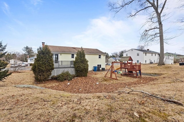 back of house with a chimney, a wooden deck, and a playground