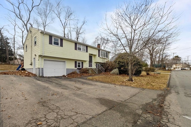 bi-level home featuring aphalt driveway, a chimney, and a garage