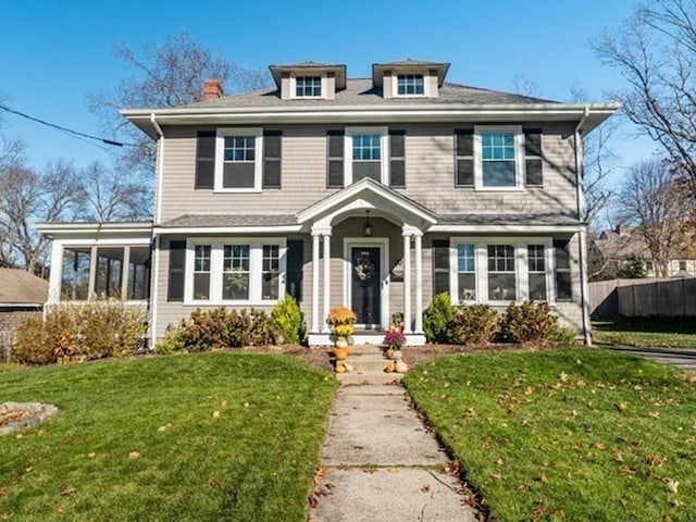 american foursquare style home featuring a front lawn, fence, and a sunroom