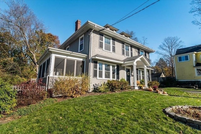 american foursquare style home with a sunroom, a chimney, and a front yard